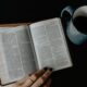 person reading book beside white ceramic mug with coffee