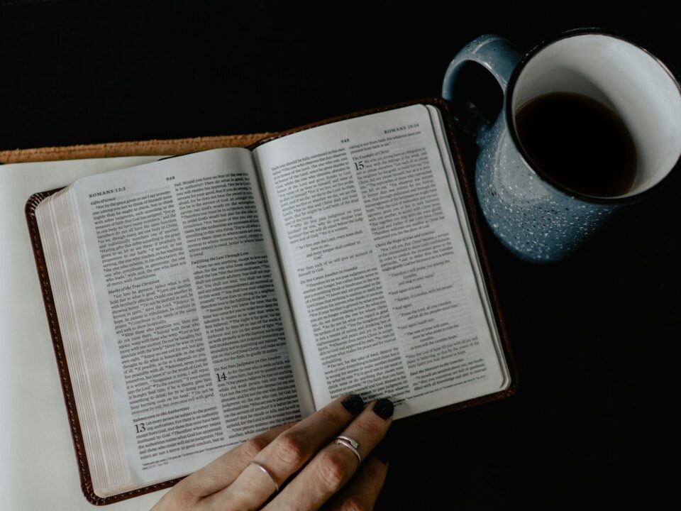 person reading book beside white ceramic mug with coffee