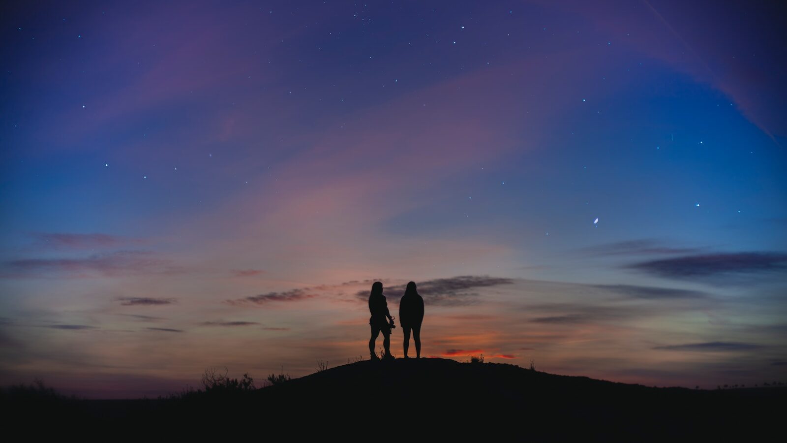 silhouette of 2 person standing on hill during night time