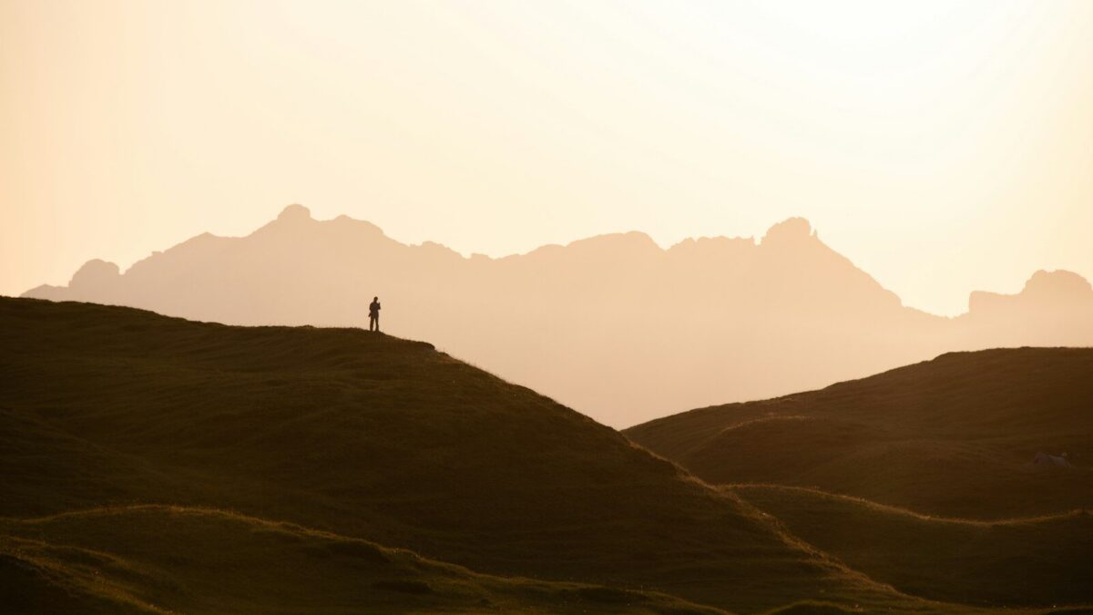A person in silhouette on a grassy hill against a warm orange sky