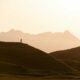 A person in silhouette on a grassy hill against a warm orange sky