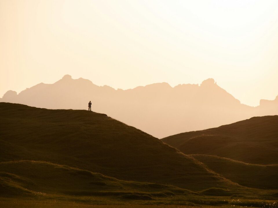 A person in silhouette on a grassy hill against a warm orange sky