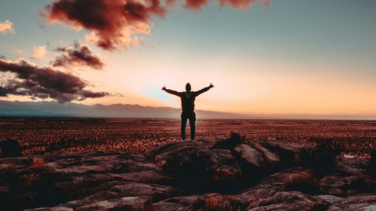 person standing on rock raising both hands