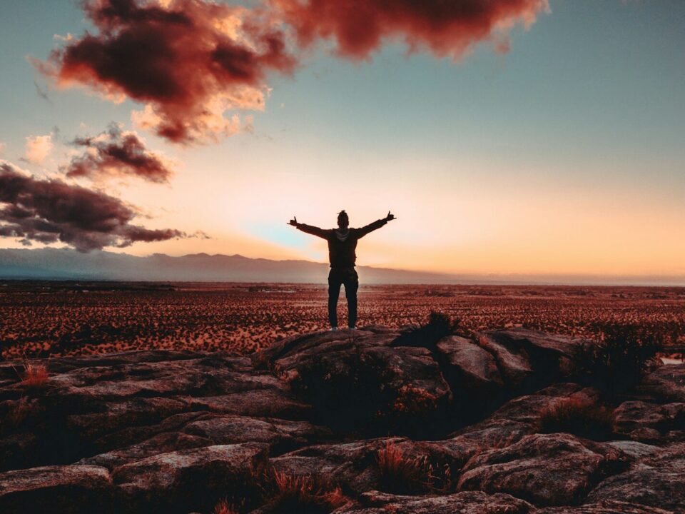 person standing on rock raising both hands