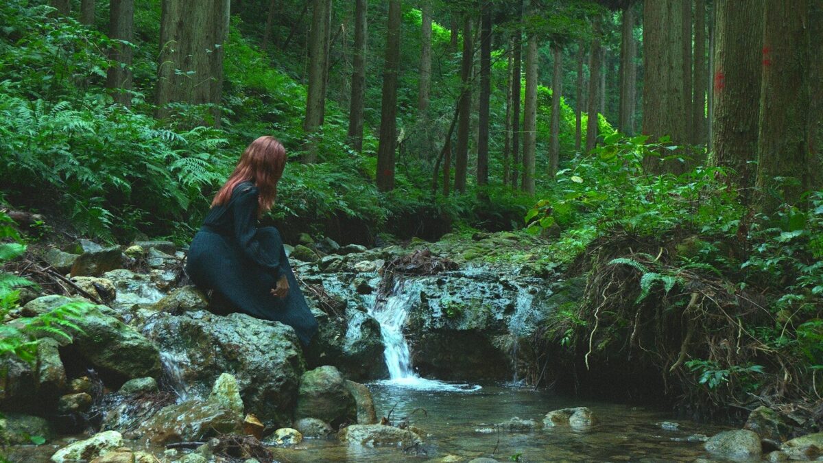 A person in a black dress on a rock by a forest stream