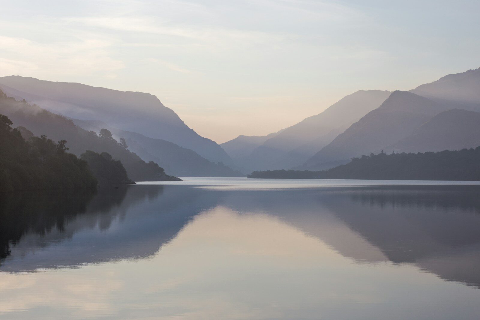 A still mountain lake reflecting misty peaks at dawn