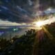 sun rays peak through clouds over herd of goats on hill
